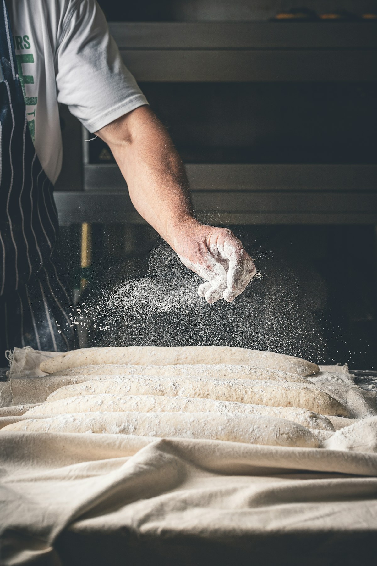 Baker dusting flour over freshly shaped loaves