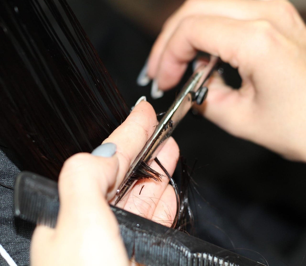 A stylist's hands cutting dark hair over a comb