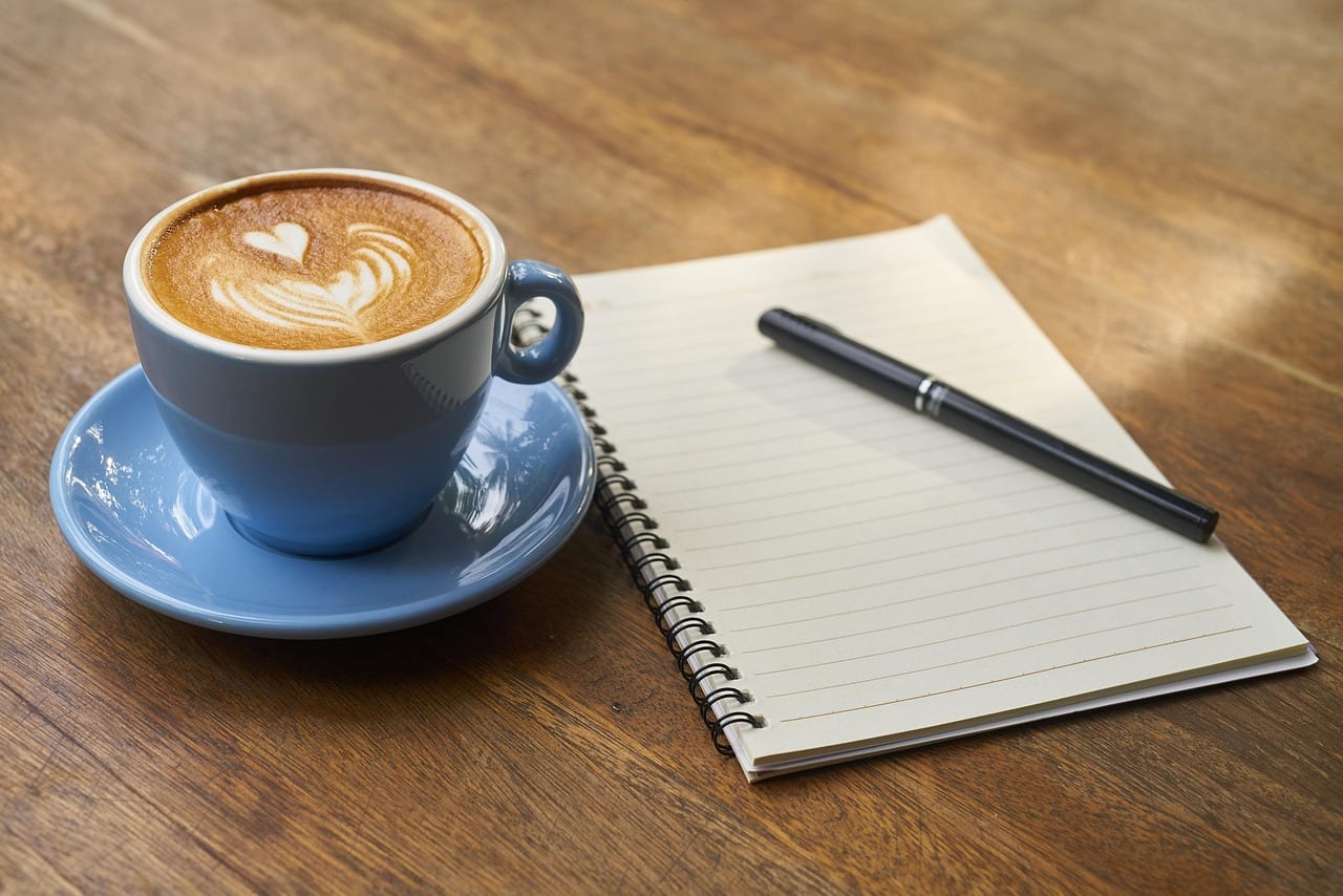 A cup of coffee next to a notebook and pen