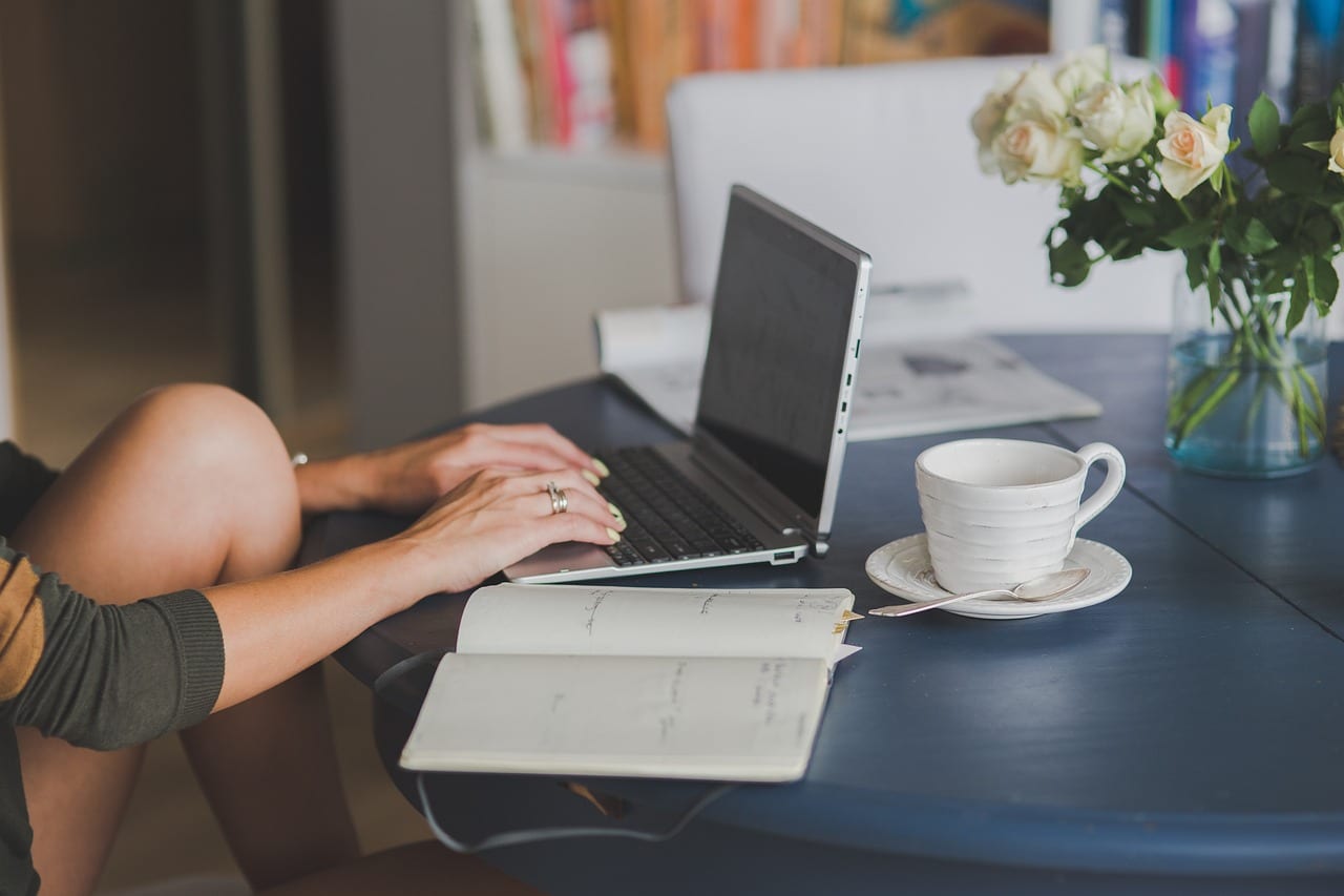Hands on a laptop next to a planner, a cup of coffee and roses